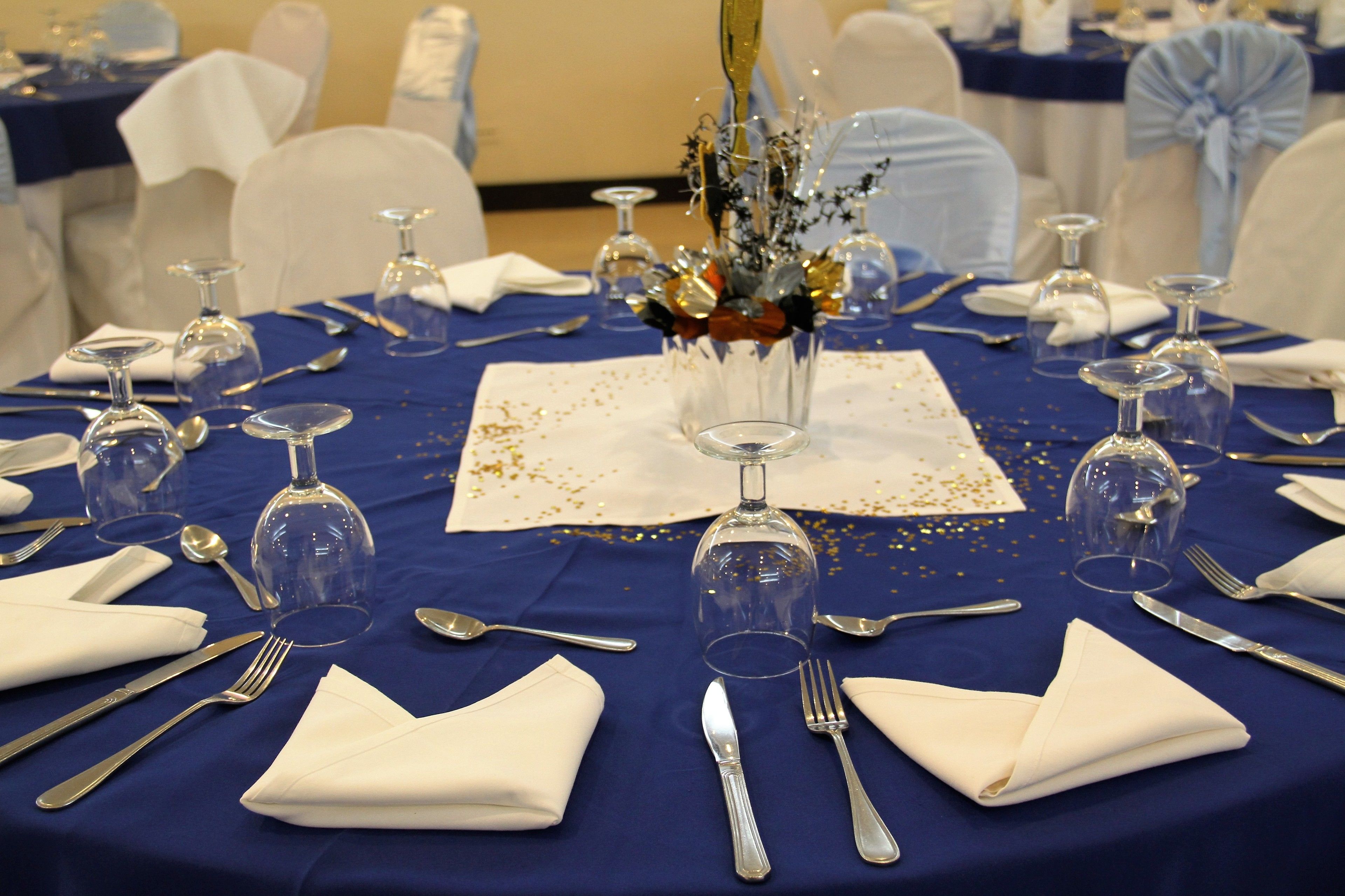 Una mesa dispuesta para un evento formal, con mantel azul, servilletas blancas y cristalería transparente.
