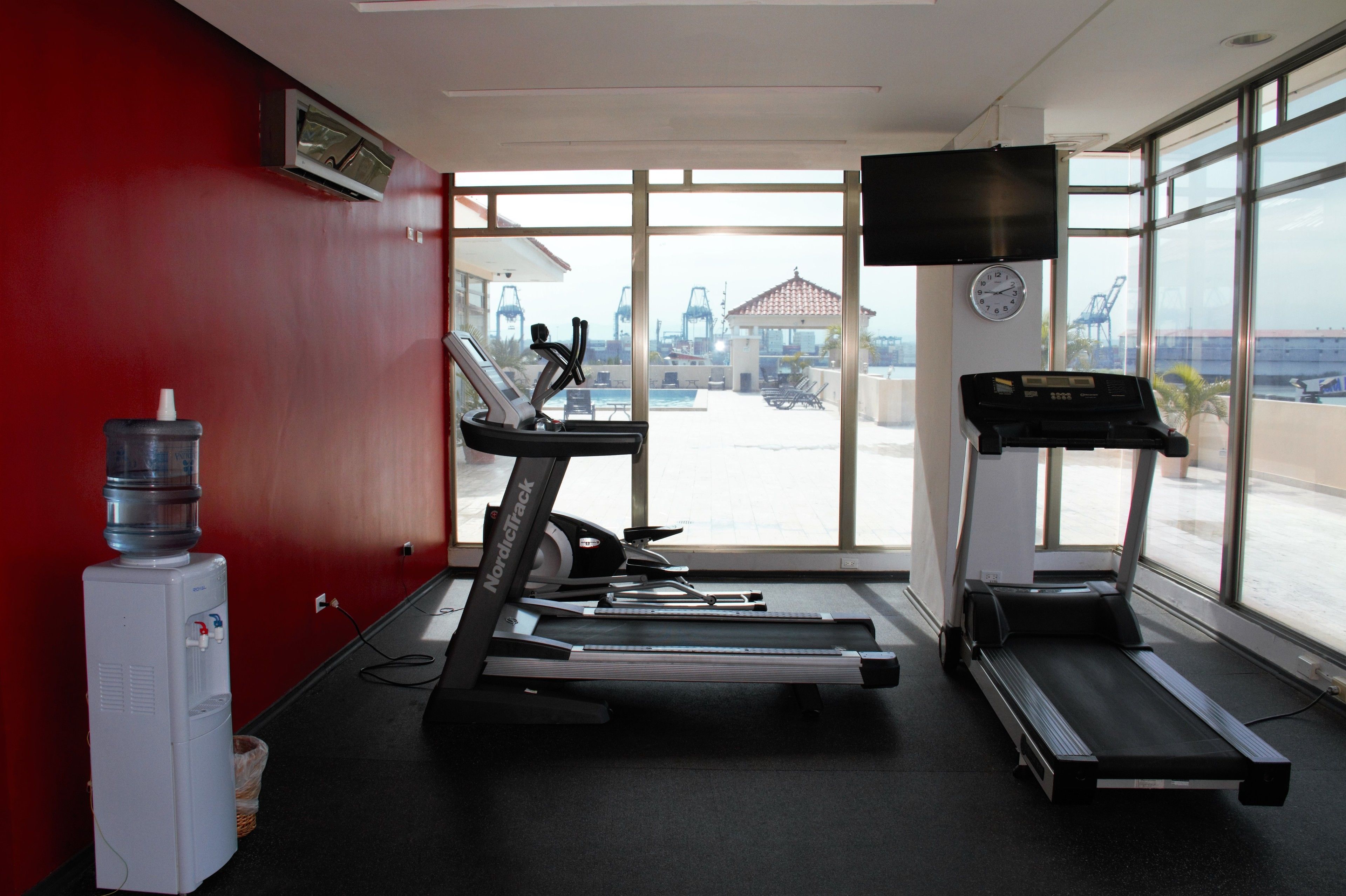 A gym with treadmills, a water dispenser, and a TV on the wall.