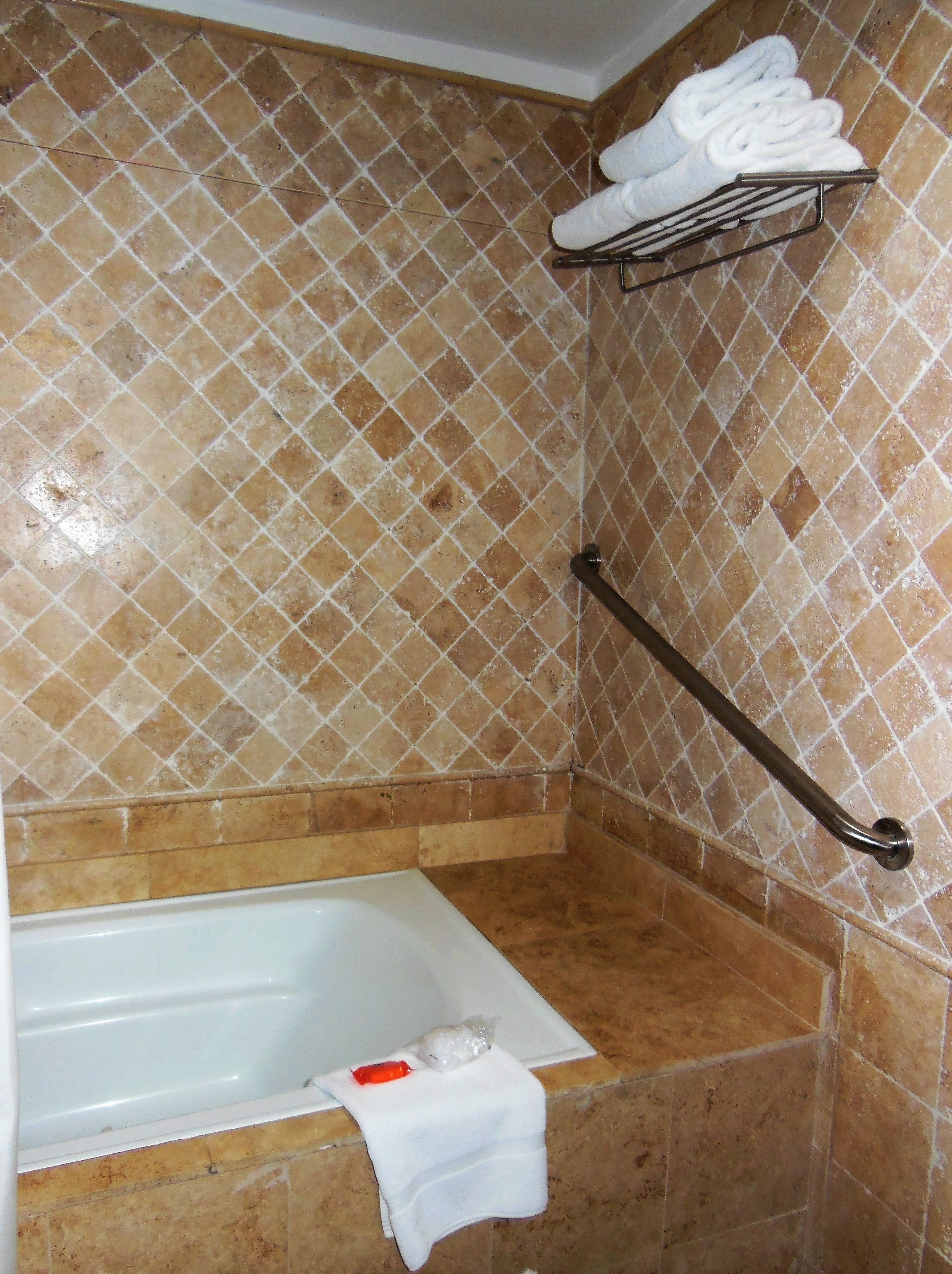 A bathroom with a bathtub, a towel rack with folded towels, and a grab bar.