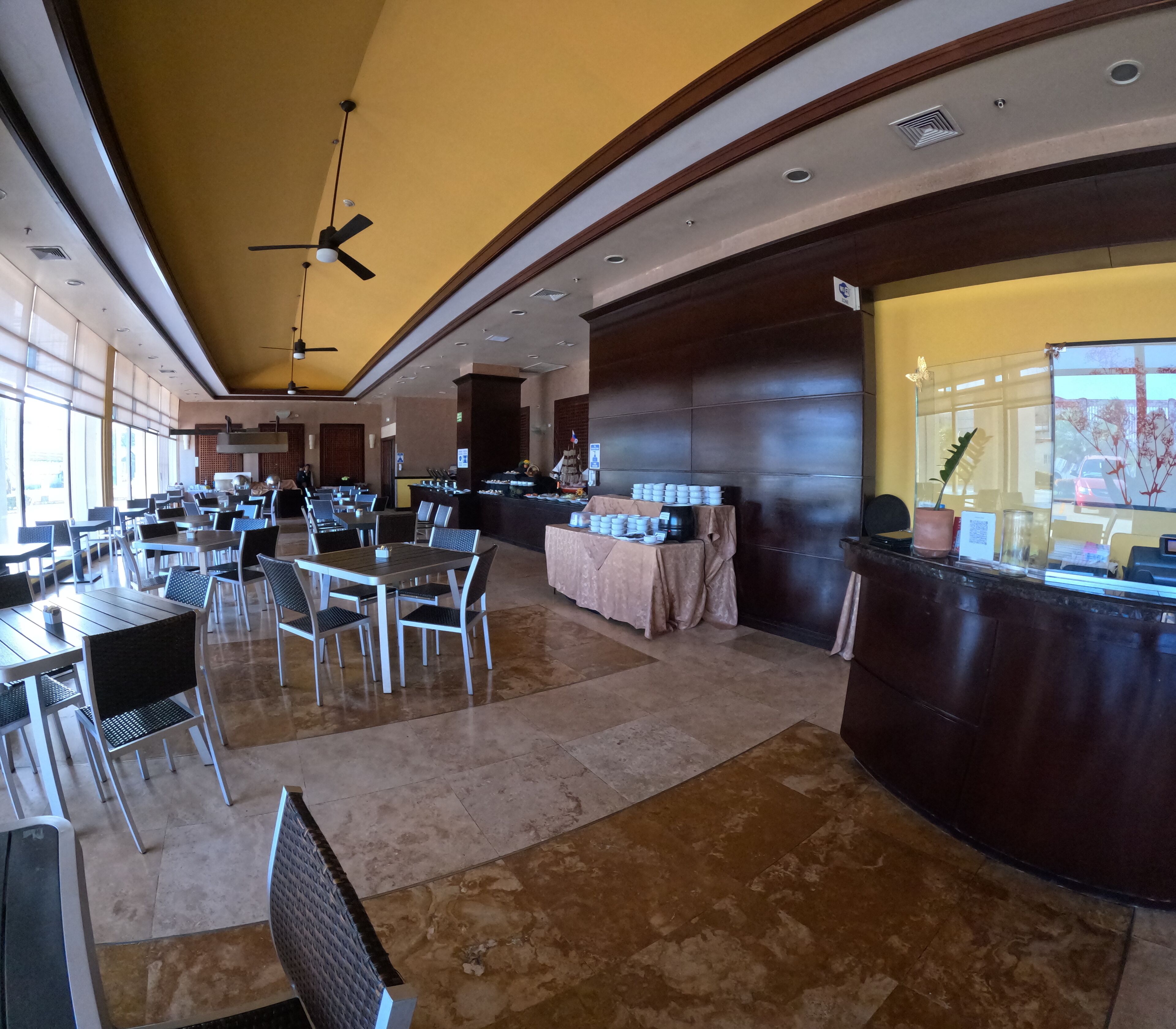 A spacious restaurant with high ceilings, large windows, and a central counter with a variety of food items.