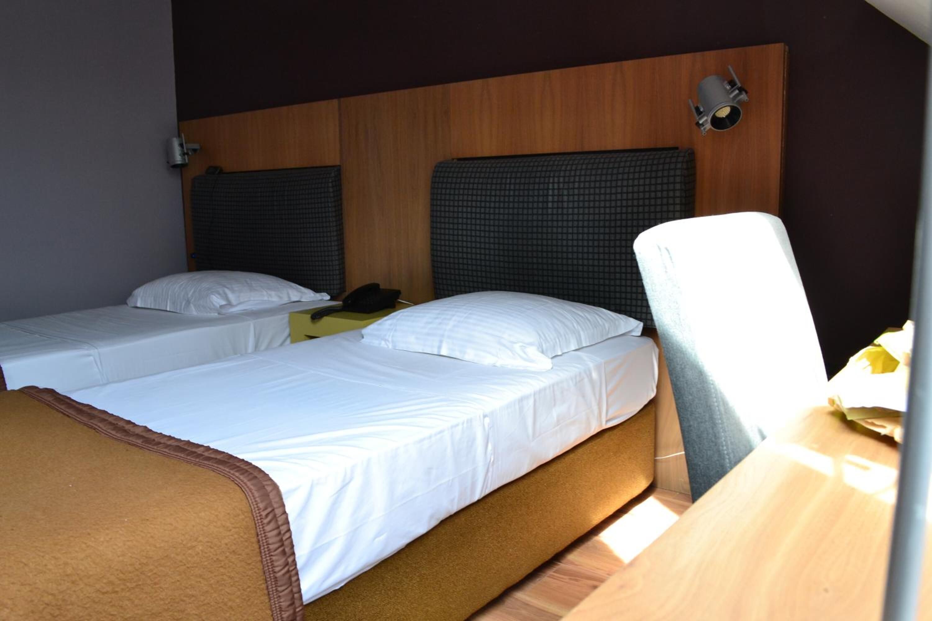 Een hotelkamer met twee enkele bedden, een houten hoofdbord, een bureau met stoel, en een wandlamp.