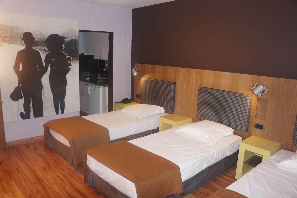 A hotel room with two single beds, a wooden headboard, a small kitchenette, and a wall-mounted TV.