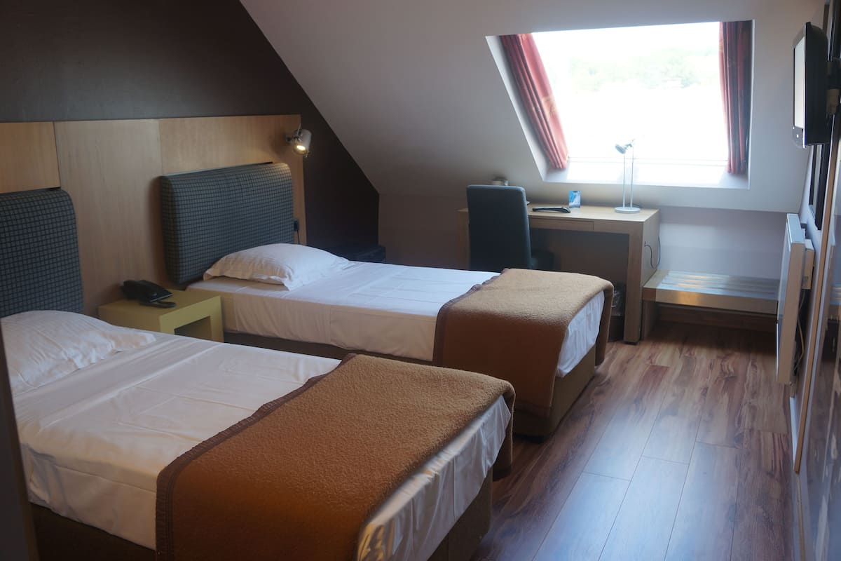 A hotel room with two beds, a desk, a chair, and a window with curtains.