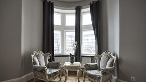 Una habitación de esquina con dos sillones decorativos, una mesita y un ventanal con cortinas.