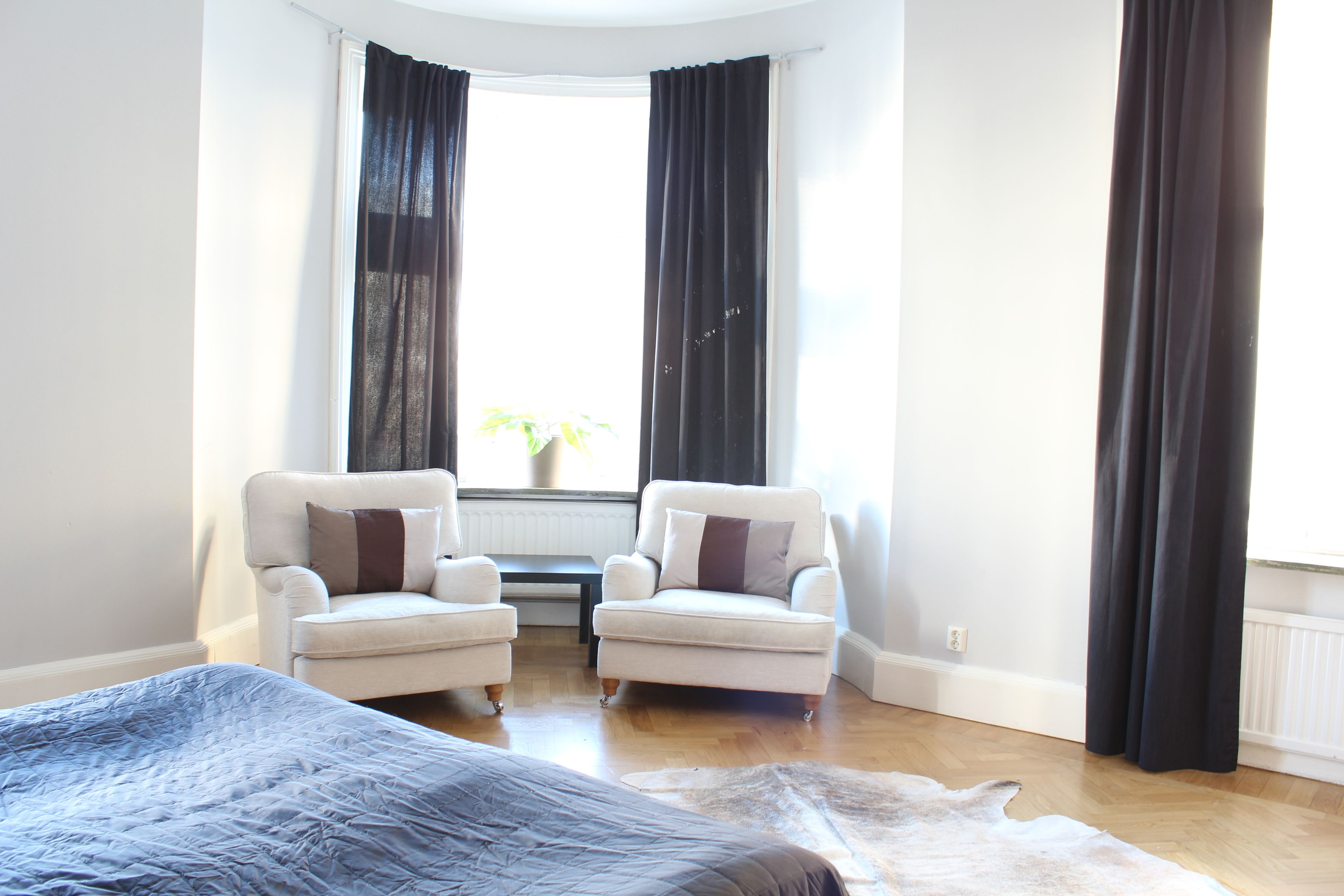 A bedroom with a large bed, two armchairs, a small table, and a window with curtains.