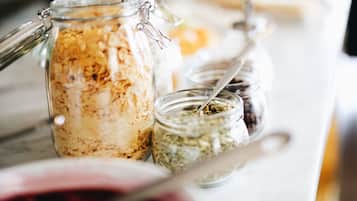 Diversos alimentos en recipientes de vidrio sobre una mesa, incluyendo un frasco con cierre metálico y una cuchara.