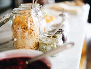 Diversos alimentos en recipientes de vidrio sobre una mesa, incluyendo un frasco con cierre metálico y una cuchara.