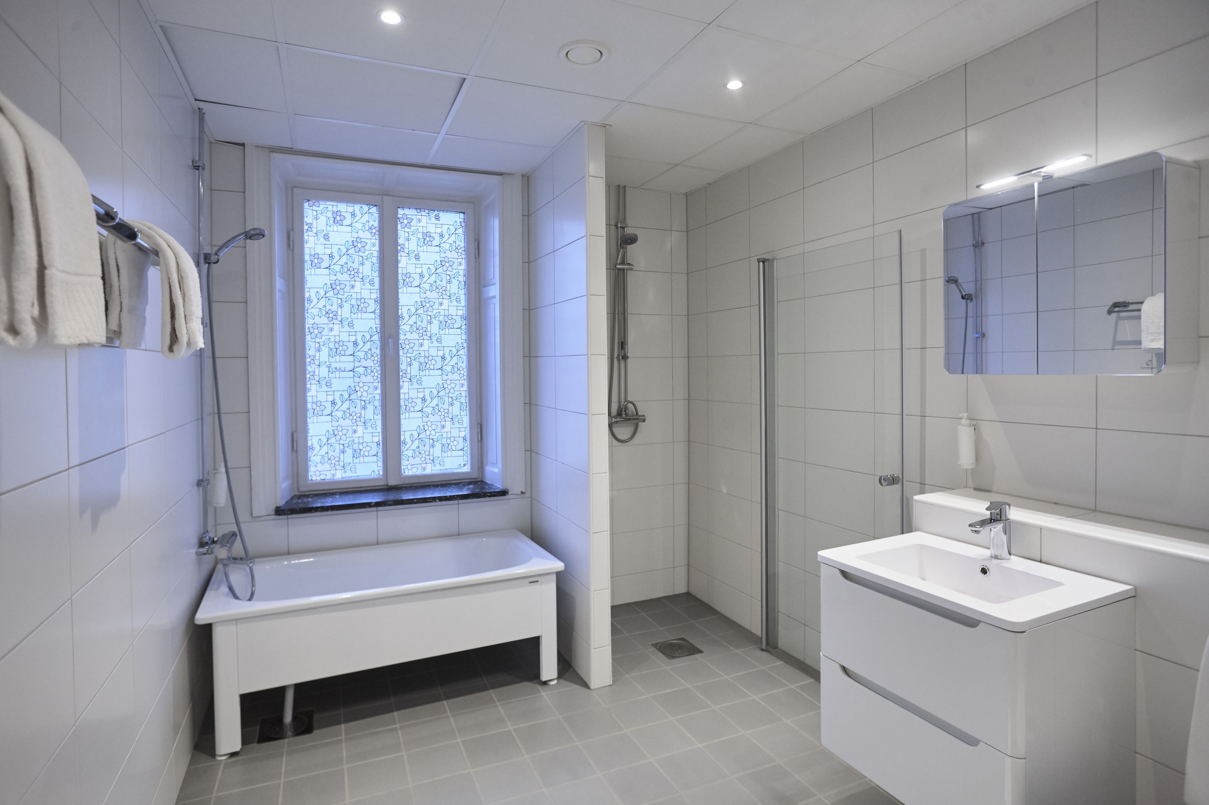 A modern bathroom with a bench, a shower, a sink, and a window with a frosted glass design.