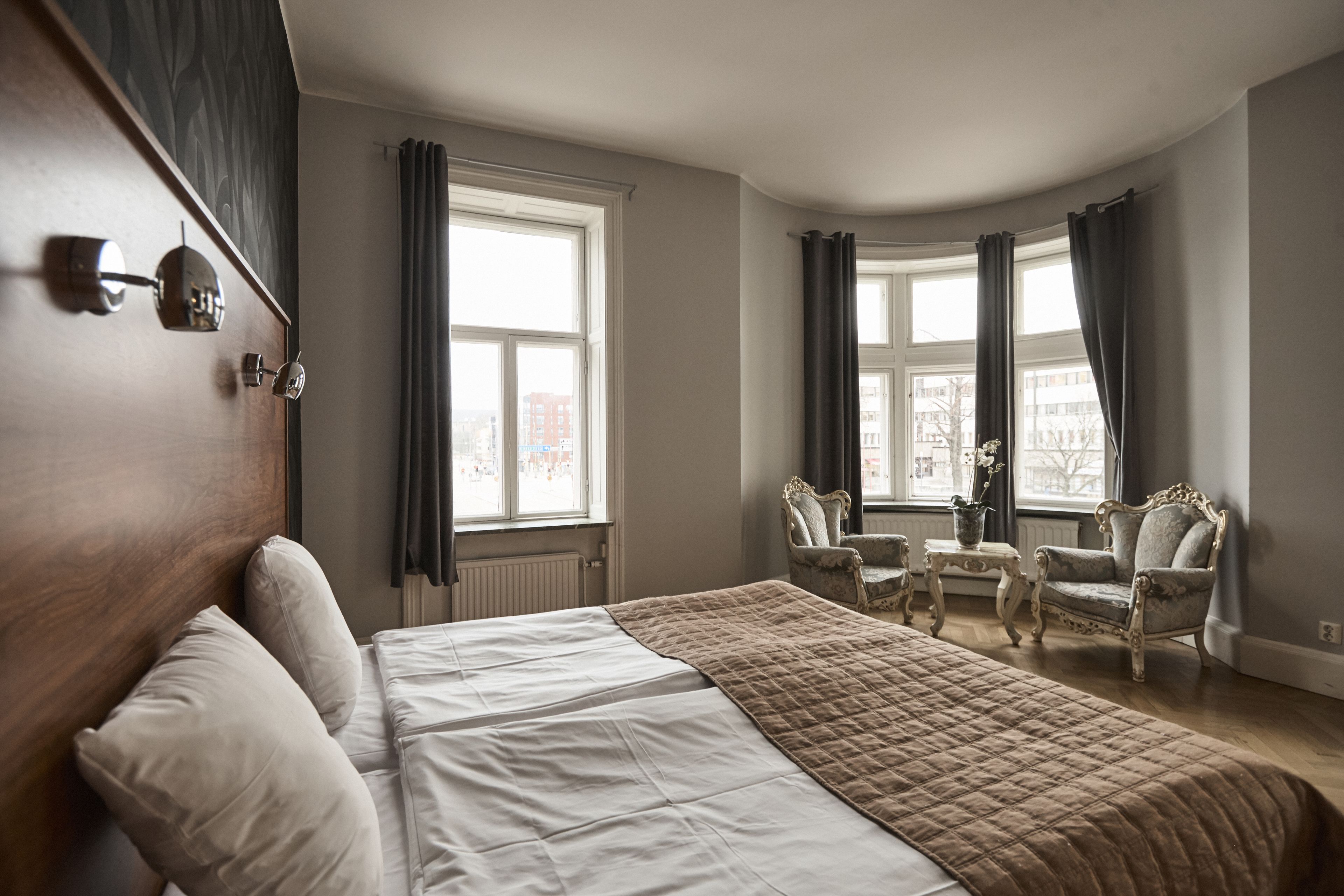 Ett hotellrum med en stor säng, två stolar, ett litet bord och ett fönster med gardiner.