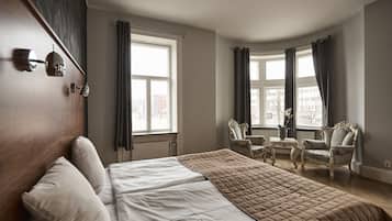 Ett hotellrum med en stor säng, två stolar, ett litet bord och ett fönster med gardiner.