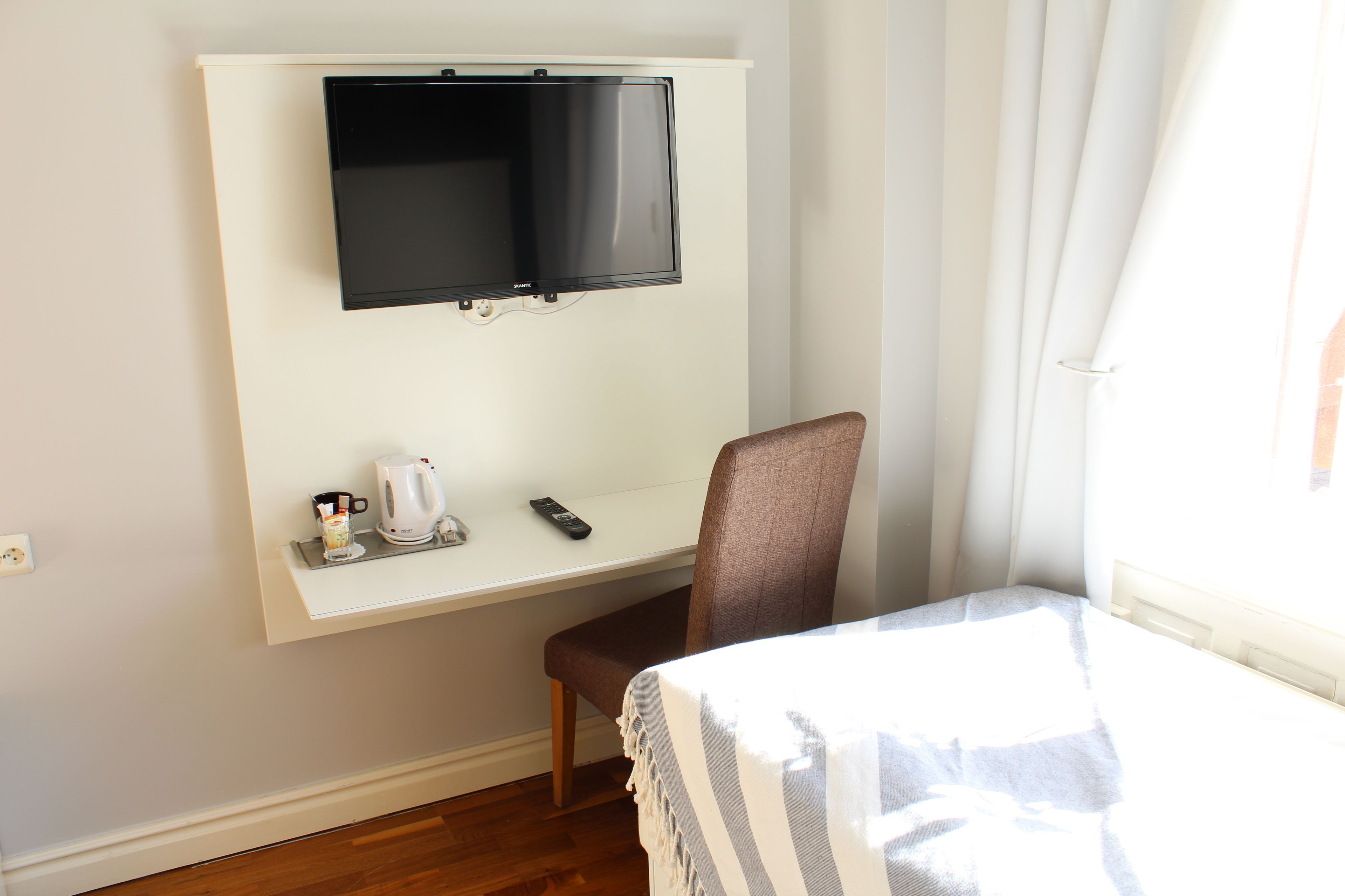 A hotel room with a bed, a TV mounted on the wall, a desk with a coffee maker, and a chair.