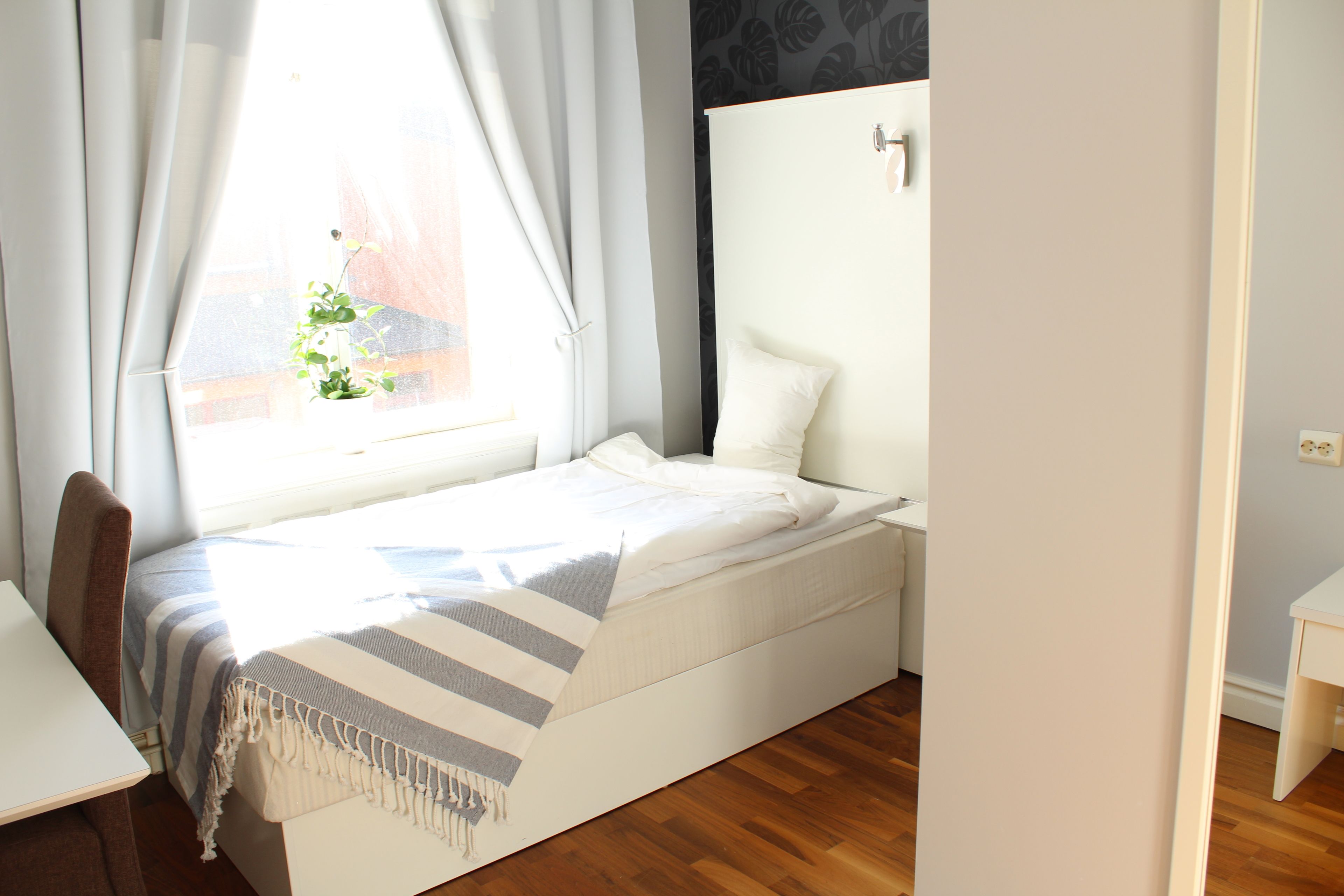 A small, neatly arranged bedroom with a bed, a desk, and a window with curtains.