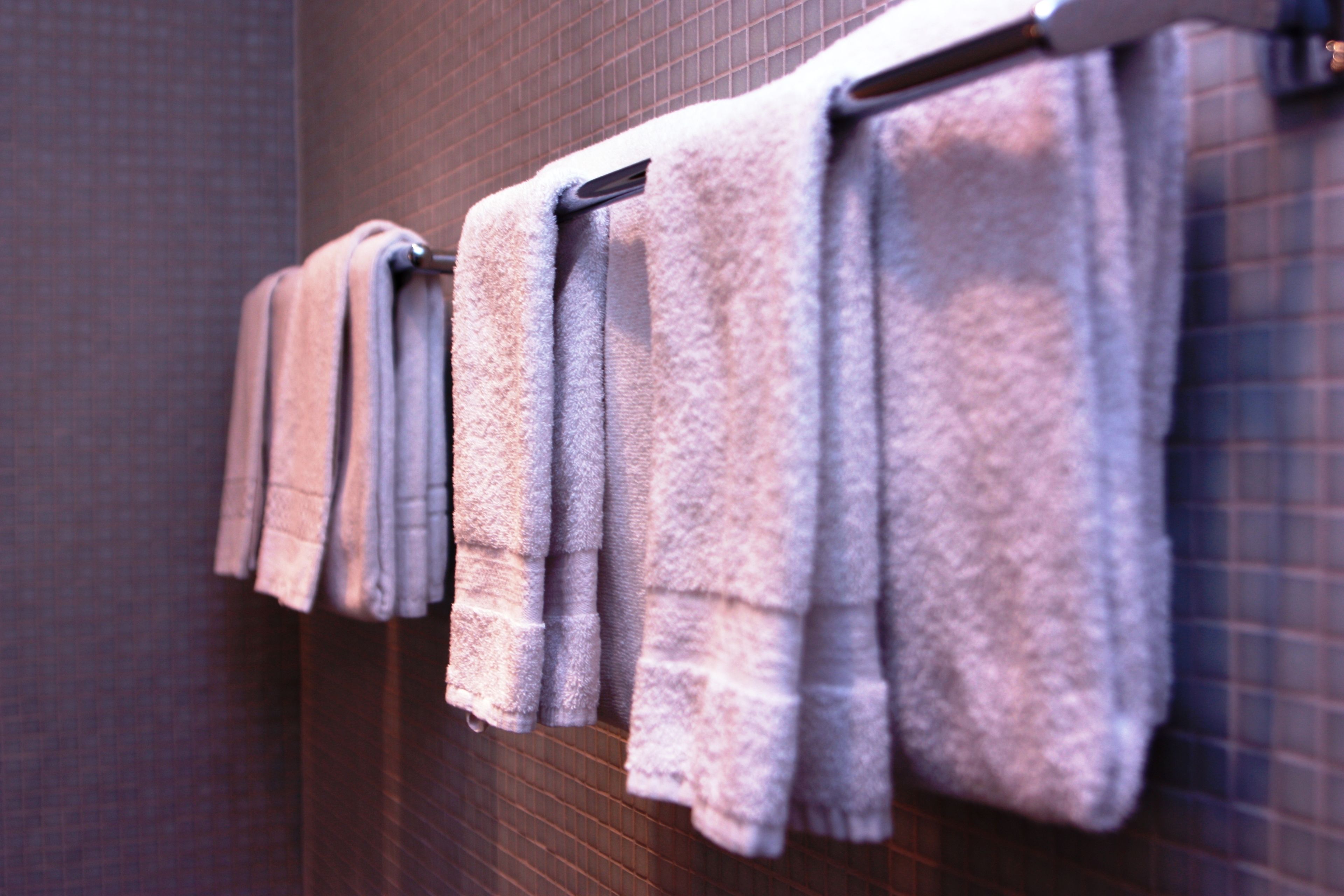 A row of neatly folded towels hanging on a rack in a bathroom with a tiled wall.