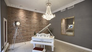Un piano de cola en una habitación con pared de ladrillo, una araña y un espejo grande.