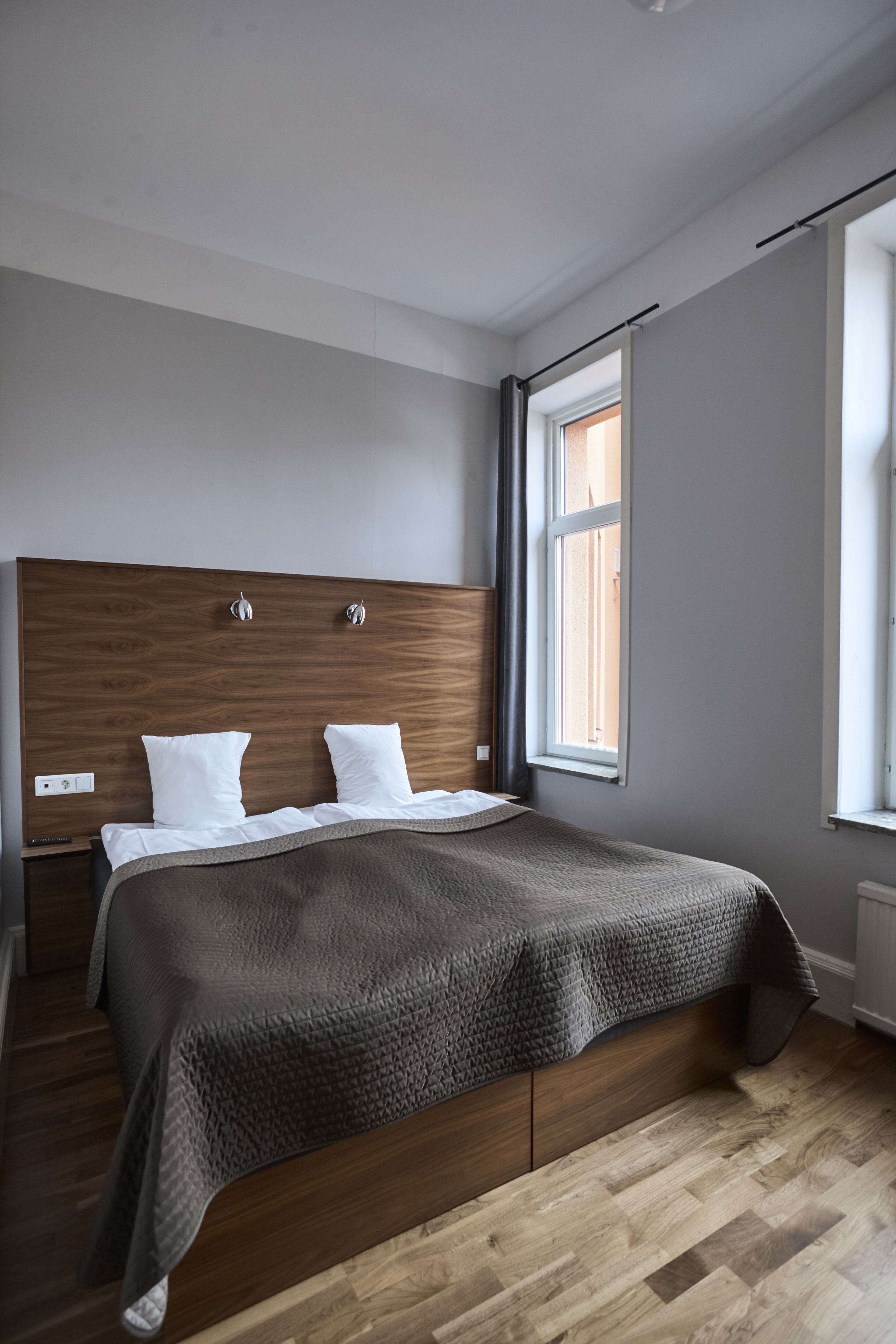 Un dormitorio moderno con cabecera de madera, un ventanal grande y una cama bien tendida.