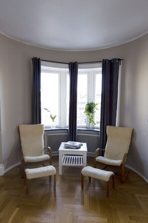 Habitación de esquina con dos sillones, una mesita y un ventanal con cortinas.
