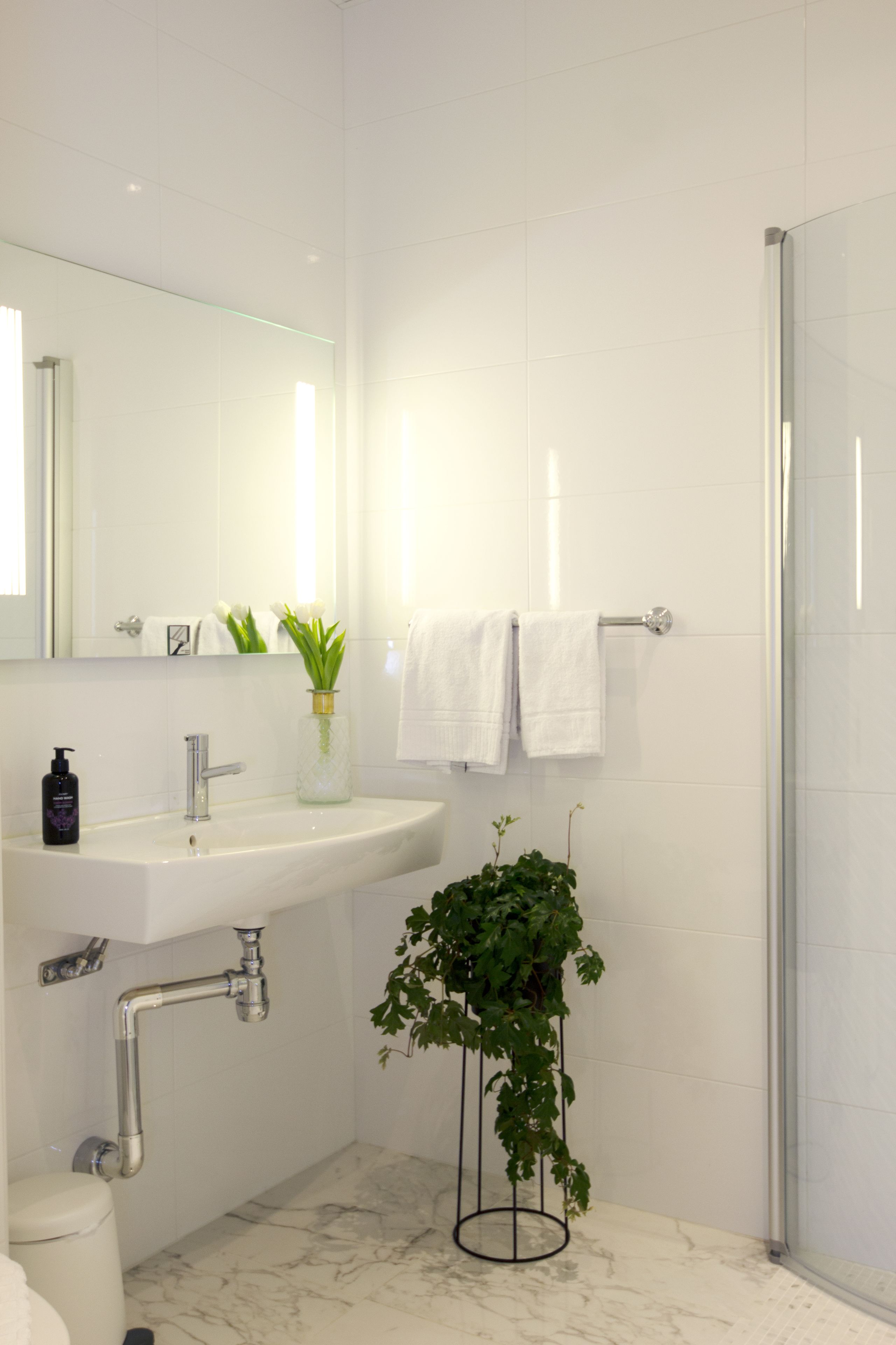 Un baño moderno con lavamanos, espejo y ducha blancos.