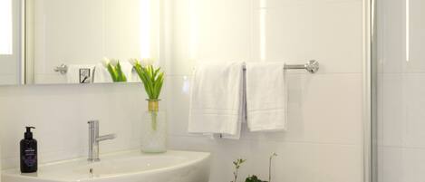 Un baño moderno con lavamanos, espejo y ducha blancos.