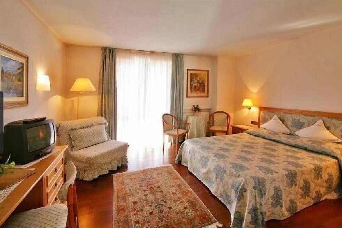 A hotel room with a bed, a sofa, a TV, a small table, and a chair.