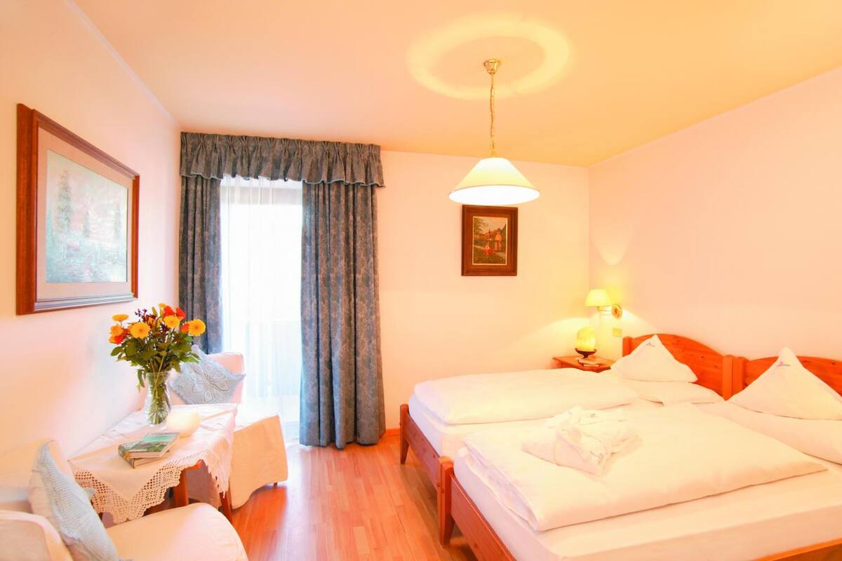 A hotel room with two beds, a desk with a chair, a vase of flowers, and a painting on the wall.