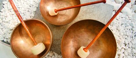 Three copper bowls with wooden mallets on a stone surface surrounded by white pebbles.