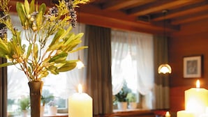 A cozy room with a wooden table, candles, and a vase with greenery. - Hotel Tschurtschenthaler (Dobbiaco)