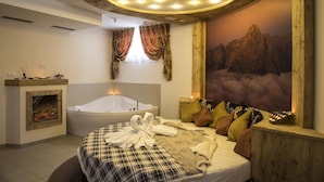 A bedroom with a large bed, a bathtub, a fireplace, and a mountain view mural. - Hotel Tschurtschenthaler (Dobbiaco)