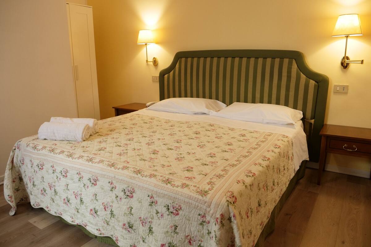 A neatly made bed with a floral bedspread, two bedside lamps, and a wooden nightstand.