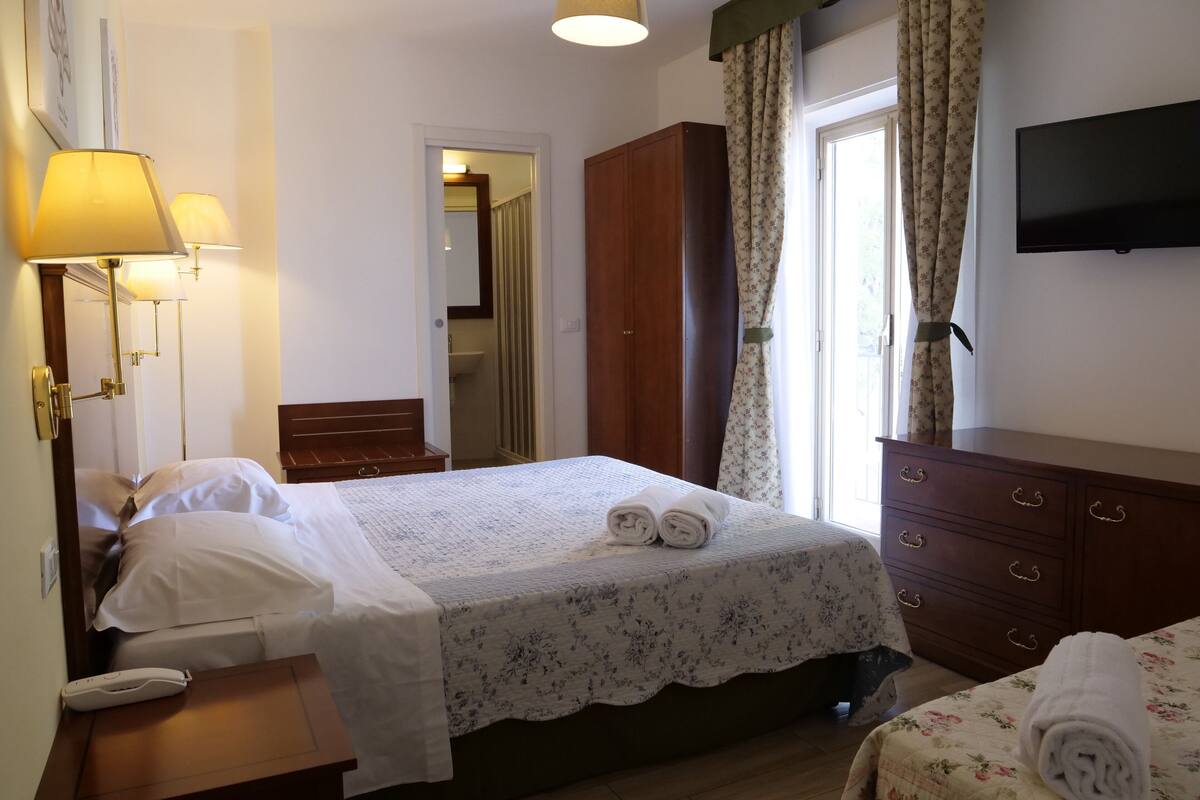A hotel room with a bed, bedside table, lamp, wardrobe, and a television on the wall.