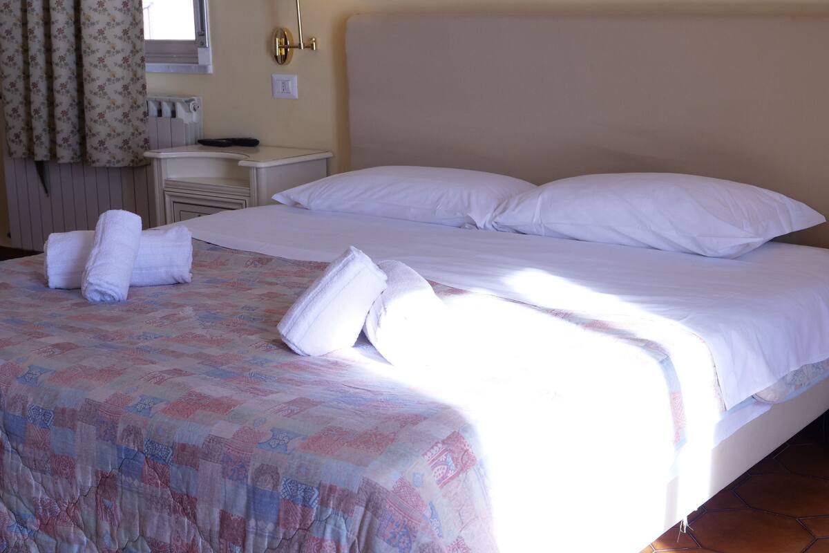 A hotel room with a large bed, a bedside table, and a window with curtains.