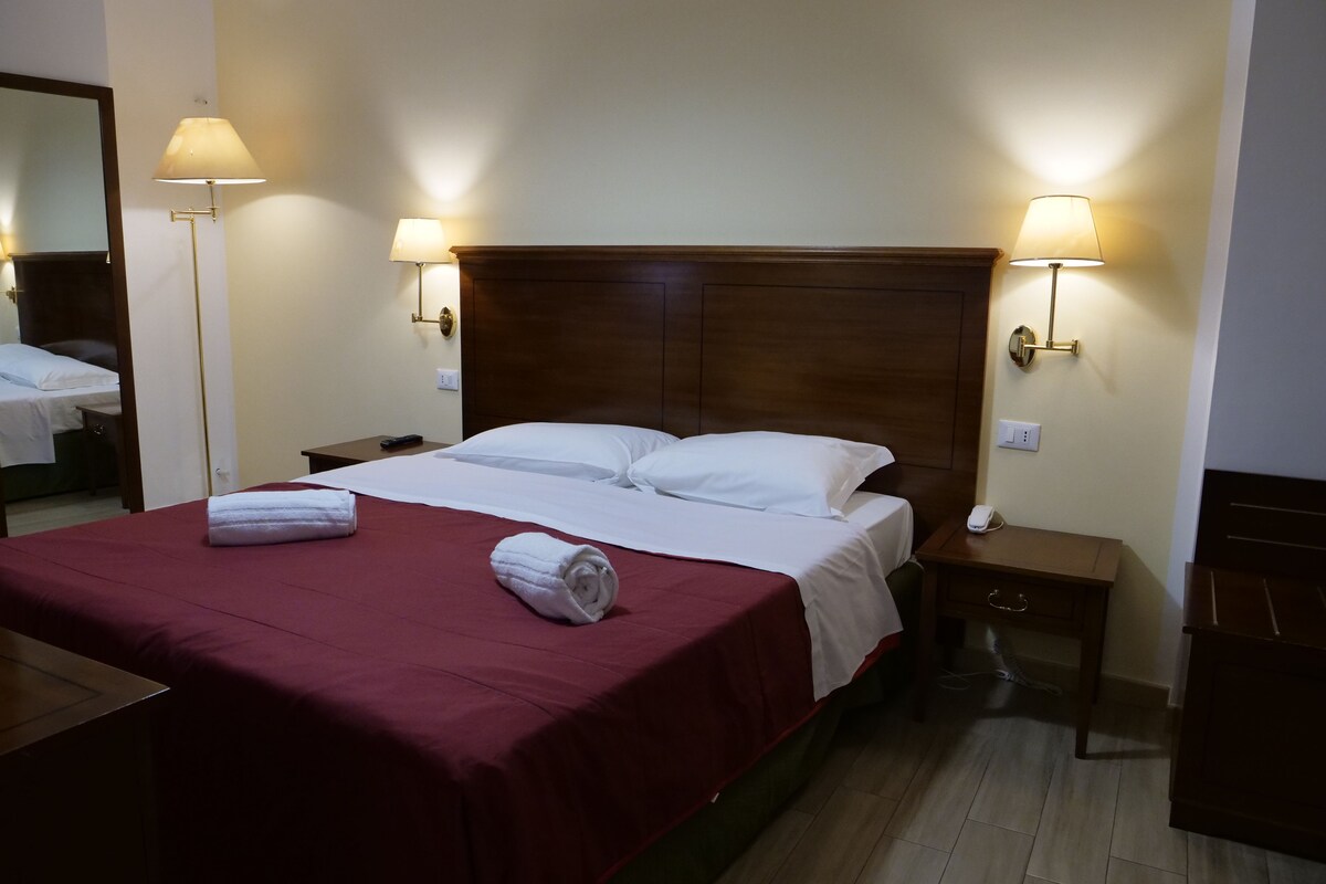 A hotel room with a large bed, two bedside lamps, a nightstand, and a wooden dresser.