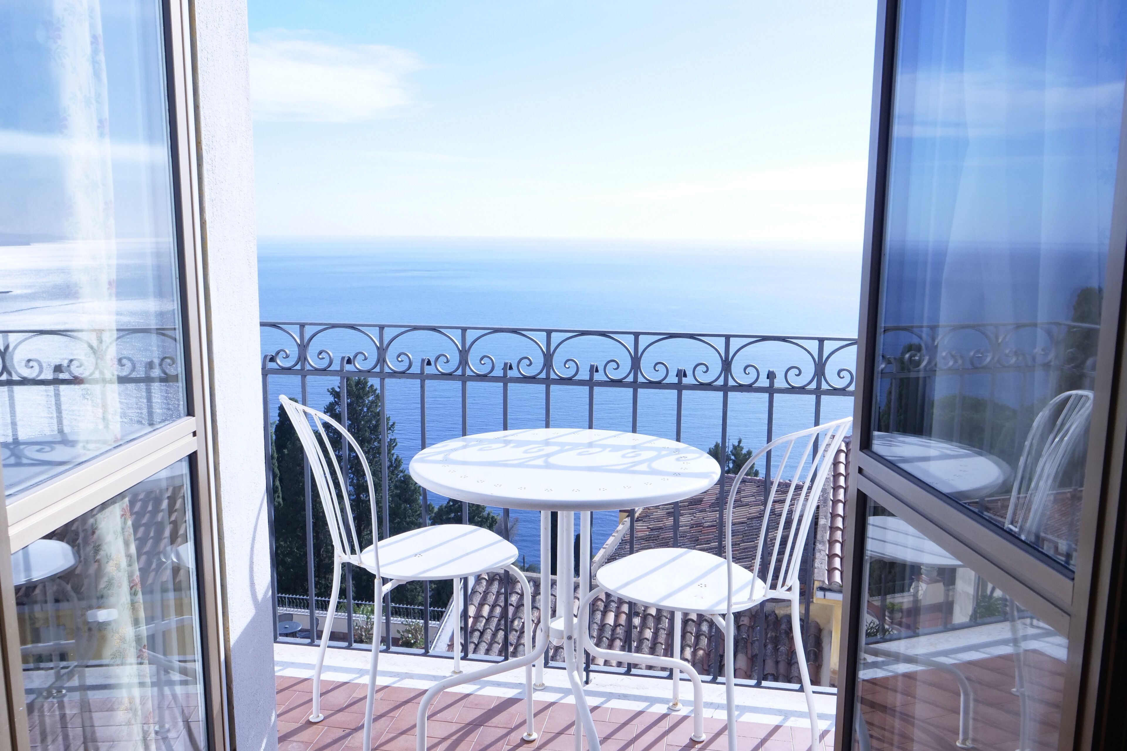 A balcony with a white table and chairs, overlooking a body of water.
