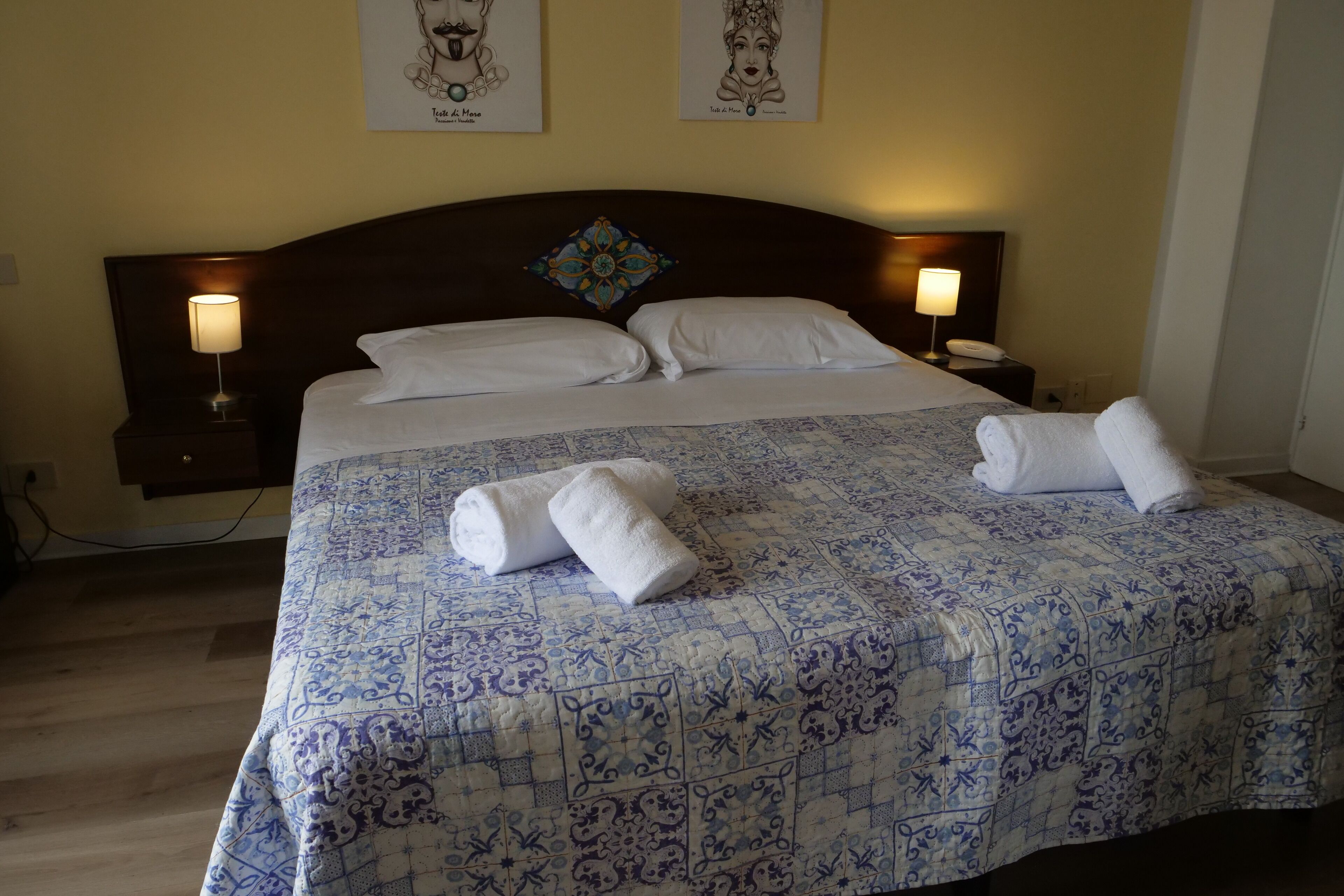 A neatly made bed with a patterned bedspread, two bedside lamps, and artwork on the walls.
