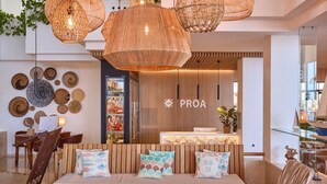 Un interior modern amb una taula de recepció de fusta, una zona de seients amb coixins estampats i llums penjants teixides.