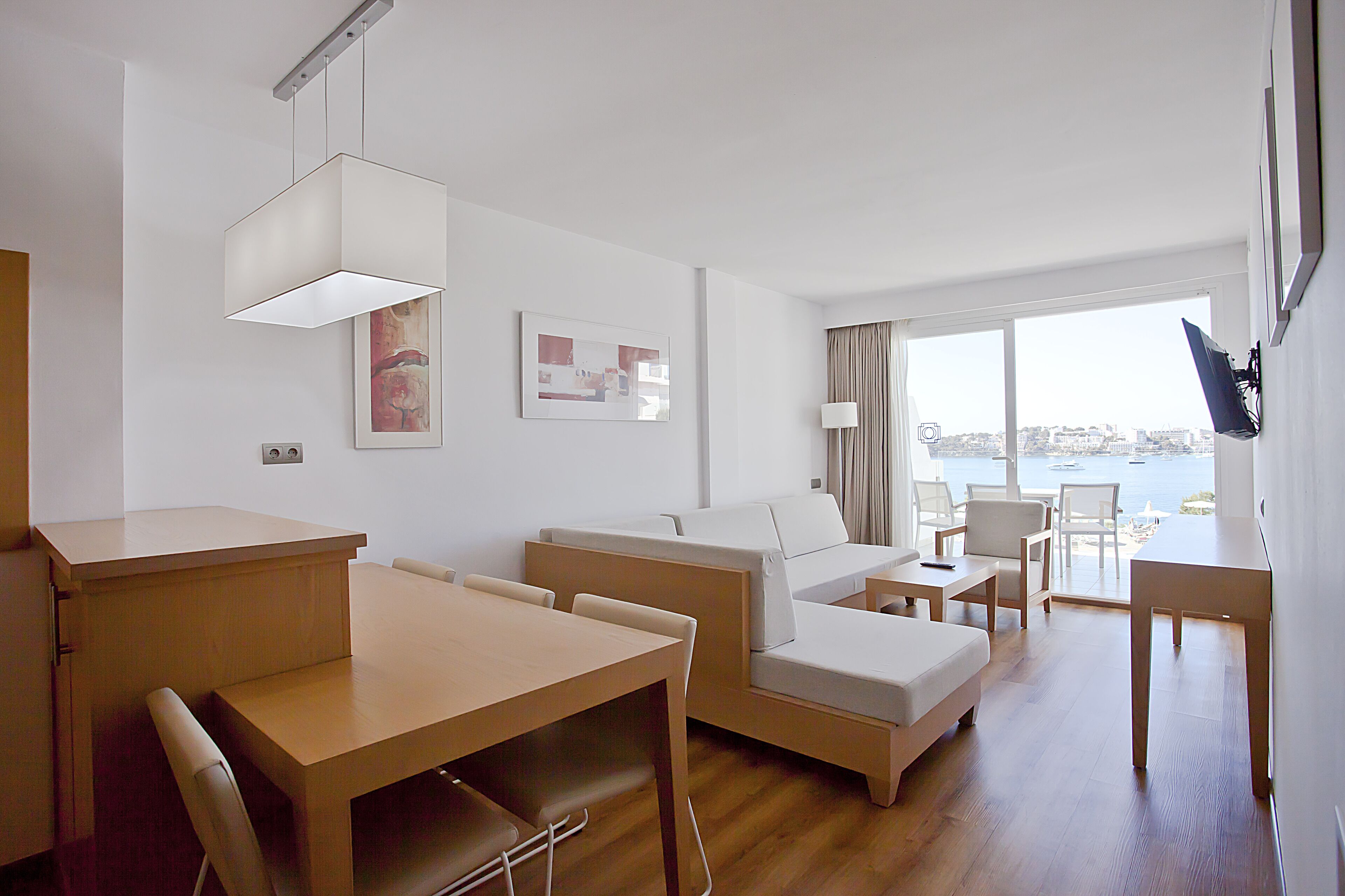 Una camera d'albergo moderna con angolo ristoro, divano, TV a parete e vista sul mare dalla finestra.