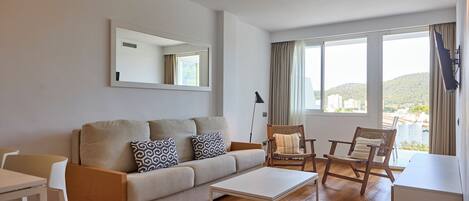 Una sala de estar moderna con un sofá, una mesa de centro y dos sillones. Un ventanal grande ofrece vistas al exterior.