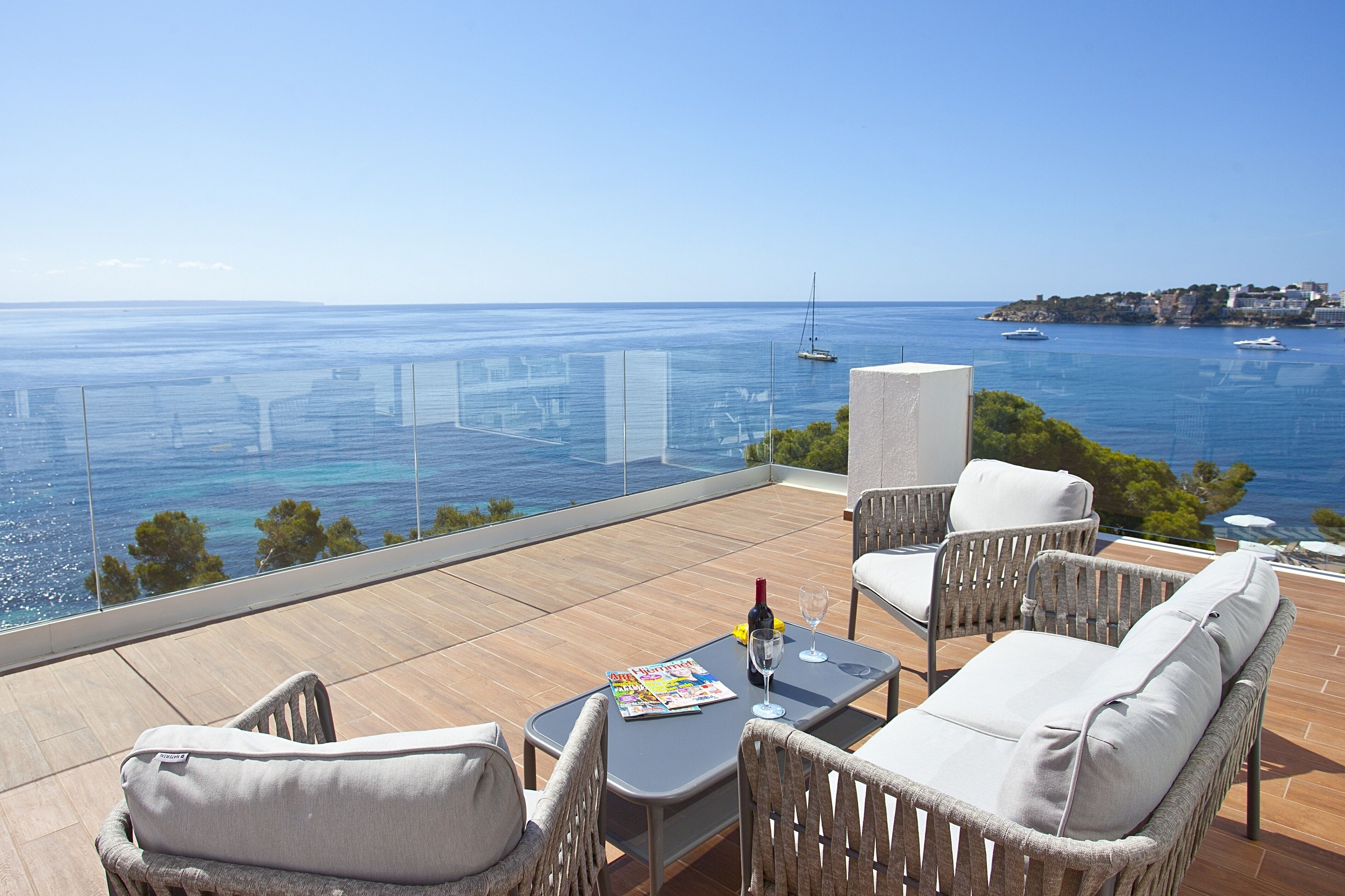 A balcony with wicker furniture, a table with a magazine, and a bottle of wine.