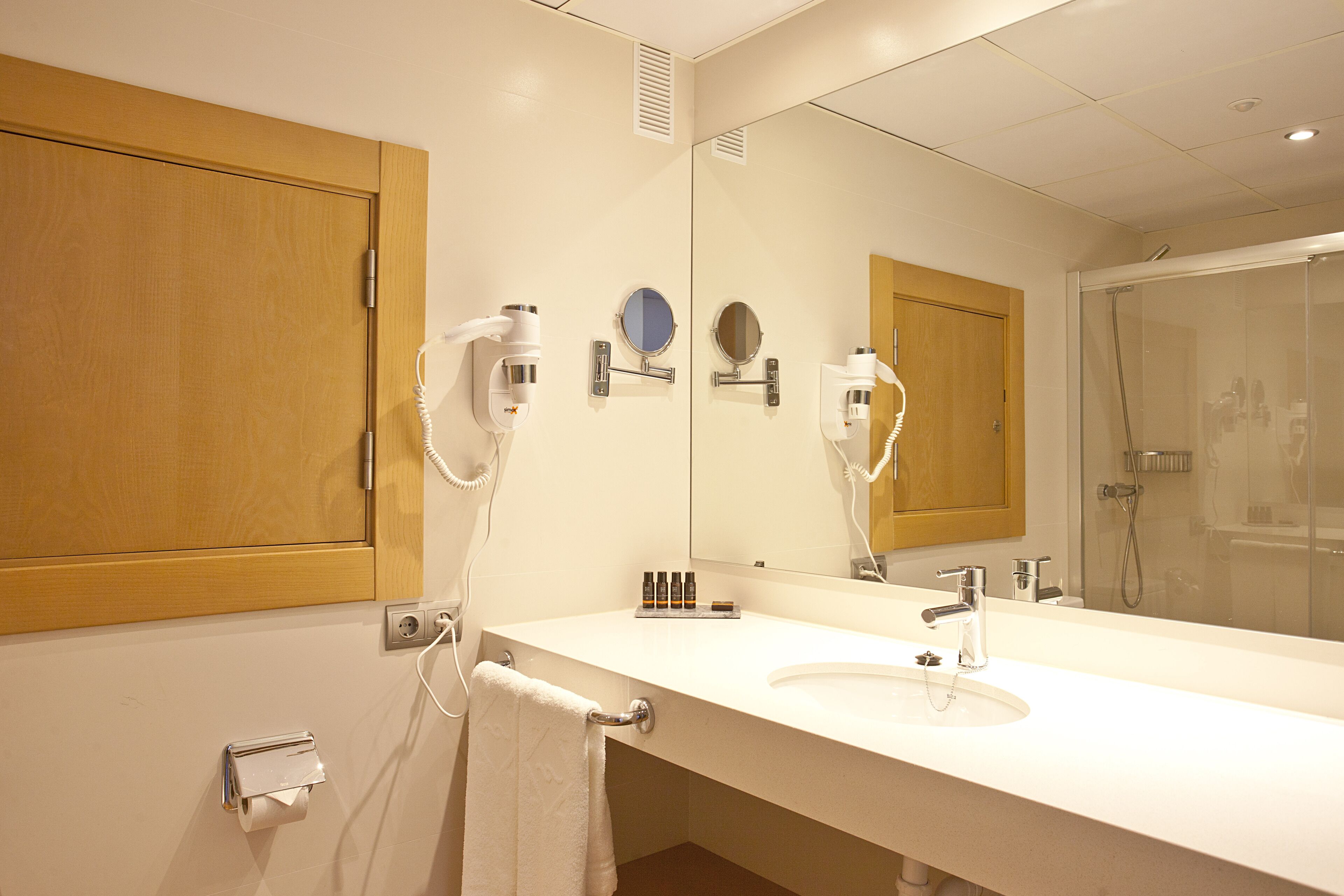 Un baño de hotel con un espejo grande, dos lavamanos, una ducha y un tendedero para toallas.