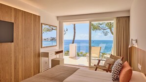 Habitació d'hotel moderna amb un llit gran, una televisió penjada a la paret i un balcó amb vista al mar.