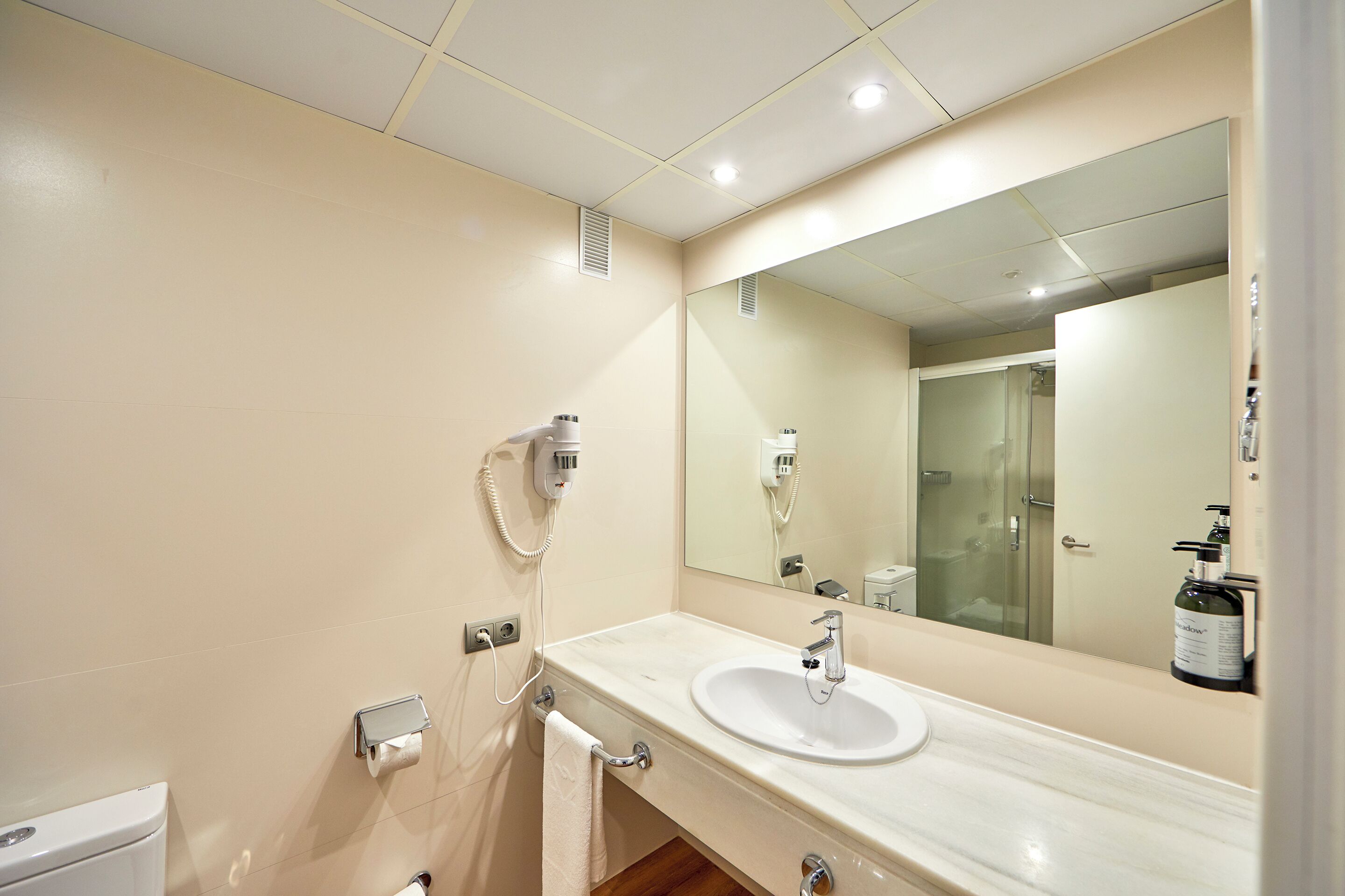 A modern bathroom with a white sink, a large mirror, and a towel rack.