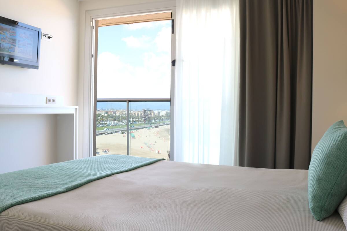 Une chambre d’hôtel avec un lit, une fenêtre donnant sur la plage, un téléviseur fixé au mur et une lampe.