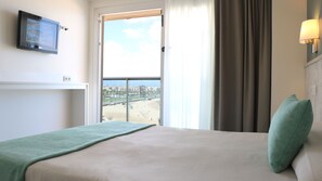 A hotel room with a bed, a window with a beach view, a wall-mounted TV, and a lamp. - Golden Donaire Beach (Salou)