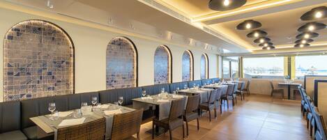 Un restaurante con mesas largas, sillas de mimbre y ventanas en arco.