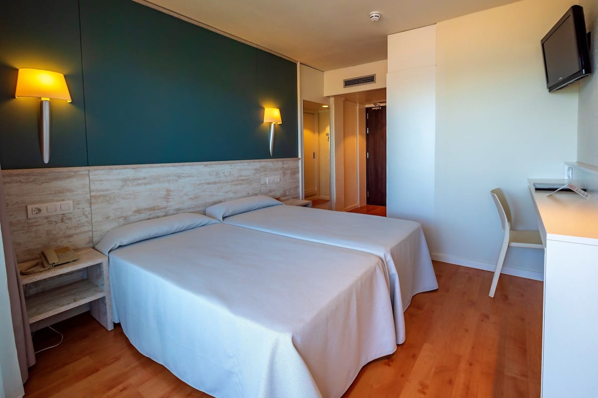 Une chambre d’hôtel avec deux lits, un bureau, une chaise, une télévision et un téléphone sur la table de chevet.