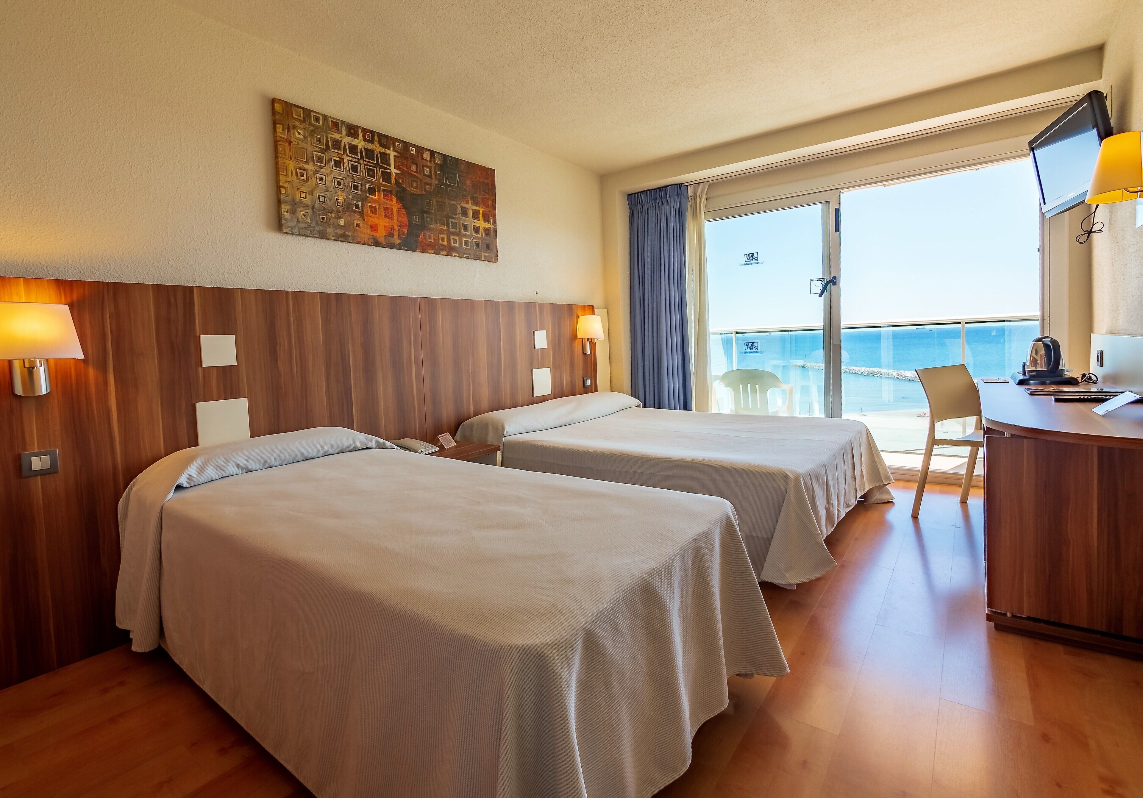 Habitación de hotel con dos camas, un escritorio, una silla, un televisor y vista al mar.