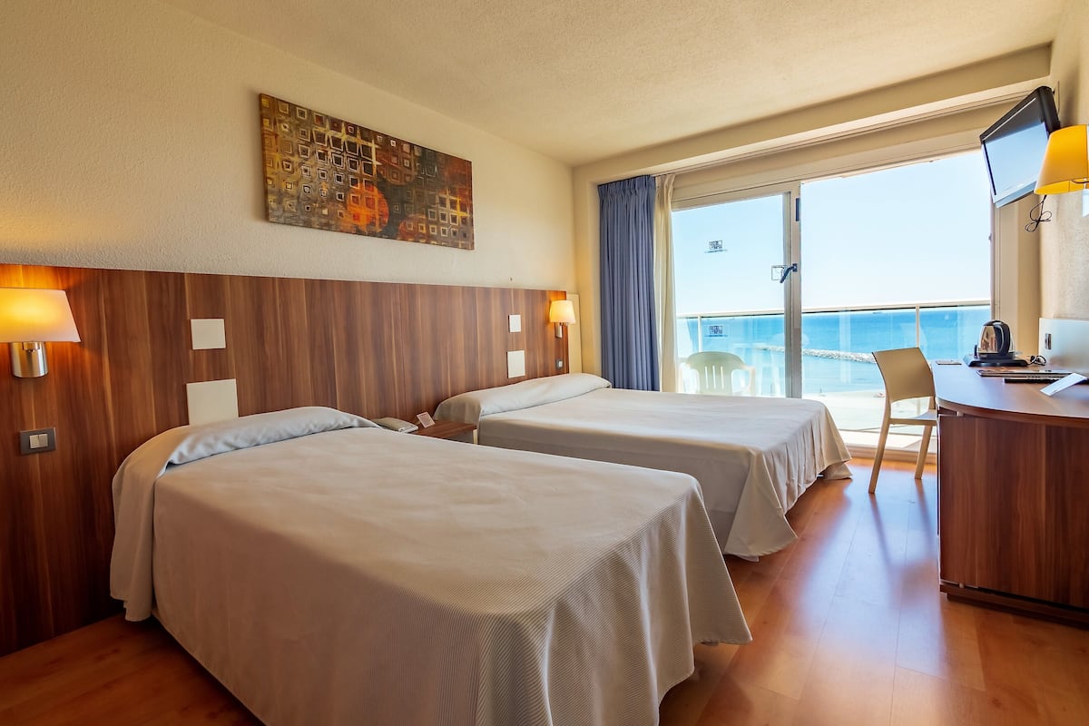 Une chambre d’hôtel avec deux lits, un bureau, une chaise, une télévision et une vue sur la mer.
