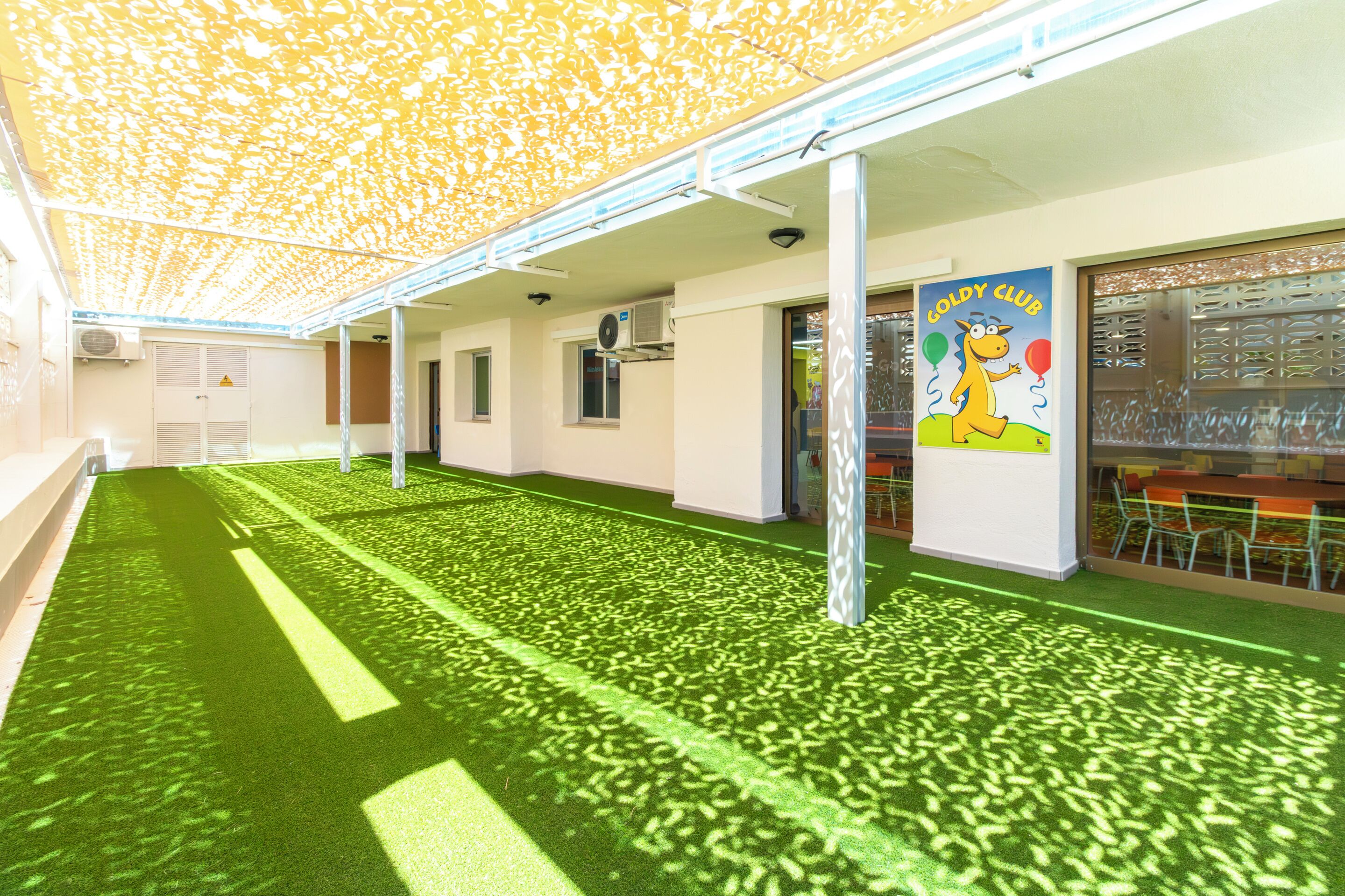 A covered outdoor area with artificial grass, columns, and a Coldy Club sign.