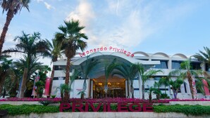 Exterior del hotel Leonardo Privilege, con un arco destacado, palmeras y un jardín bien cuidado.