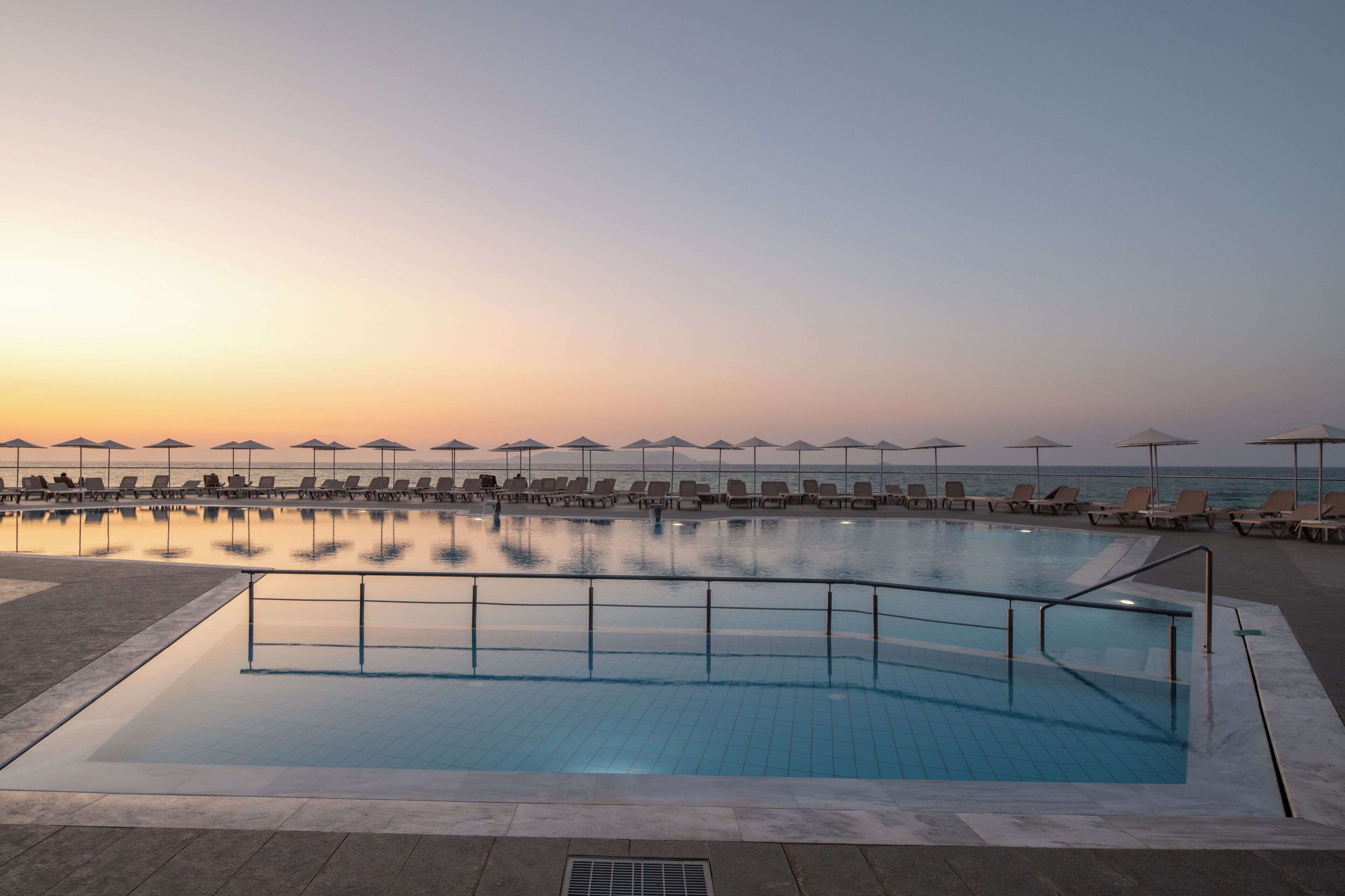 Ein Schwimmbecken mit Liegestühlen und Sonnenschirmen mit Blick aufs Meer.