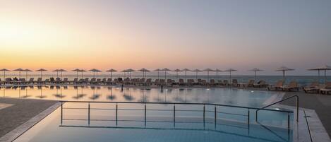A swimming pool with lounge chairs and umbrellas, overlooking the sea.